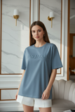 Woman wearing a blue t-shirt with embossed "PAS JALOU" text in an indoor setting