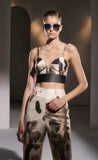 Model wearing a patterned top and pants with pas jalou sunglasses in a studio setting