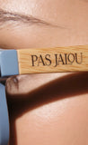 Makeup brush with 'PAS JALOU' branding on a close-up of skin.