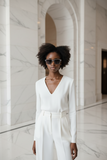 Woman in a white outfit standing in a marble hallway, wearing Pas Jalou grey sunglasses.