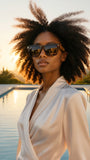 Woman with styled hair wearing pas jalou sunglasses by a pool at sunset