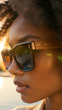 Person wearing sunglasses with 'PAS JALOU' branding, blurred background