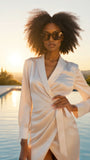 Woman in a white outfit with pas Jalou sunglasses standing by a pool at sunset.