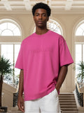 Person wearing a pink t-shirt with 'PAS JALOU' branding in an elegant interior setting.