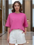 Woman wearing a pink oversized t-shirt with text and white shorts in an indoor setting.