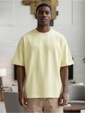 Man wearing a light yellow t-shirt with text in a modern indoor setting