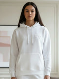 Person wearing a white hoodie with embossed text "#agoodtime" standing indoors.