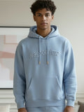 Person wearing a light blue hoodie with '#agoodtime' text in a neutral indoor setting