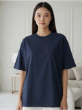 Person wearing a navy blue t-shirt with 'Pas Jalou' text in a minimalistic room.