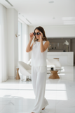 Woman in a white outfit standing in a modern, minimalistic room., Weraing Pas Jalou brown cat eye  sunglasses