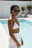 Woman in a white bikini and Pas Jalou sunglasses by a pool