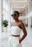 Woman in a white outfit and pas jalou sunglasses standing in a stylish interior setting