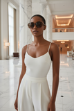 Woman in a white dress and pas jalou sunglasses standing in a modern building lobby.