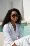 Woman in a white outfit and pas jalou sunglasses sitting by a pool.