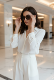 Woman in a white outfit adjusting pas jalou sunglasses in a marble hallway