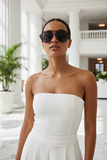 Woman wearing a strapless white dress and pas jalou sunglasses in an elegant indoor setting.