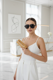 Woman in a white dress holding pas jalou sunglasses wooden case with sunglasses in a modern interior setting