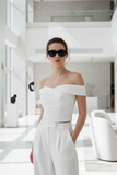 Woman in a white outfit with sunglasses standing in a modern, minimalistic room.