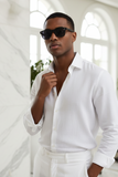 Man wearing a white shirt and pants with sunglasses in a bright room.