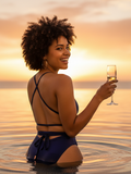 Woman in a blue swimsuit holding a glass of wine in the water at sunset.