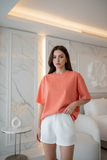 Woman wearing a coral t-shirt and white shorts in a modern room.