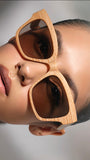 Close-up of a person wearing wooden sunglasses with a neutral background