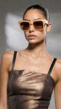 Model wearing brown sunglasses and a sheer brown top against a gray background