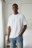 Man wearing a white t-shirt with text in a bedroom setting