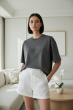 Woman wearing a gray t-shirt with 'PAS JALOU' text in a modern living room.