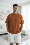 Man wearing a brown t-shirt with "pas jalou" embossed text in a modern living room