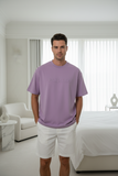 Man wearing a purple t-shirt and white shorts standing in a modern living room.