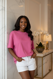 Woman wearing a pink oversized t-shirt with embossed " pas jalou" text