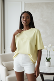 Woman wearing a light yellow oversized t-shirt with embossed "pas jalou" text