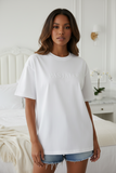 Woman wearing a white t-shirt with text in a bedroom setting