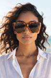 Woman wearing leopard print sunglasses and a white shirt outdoors